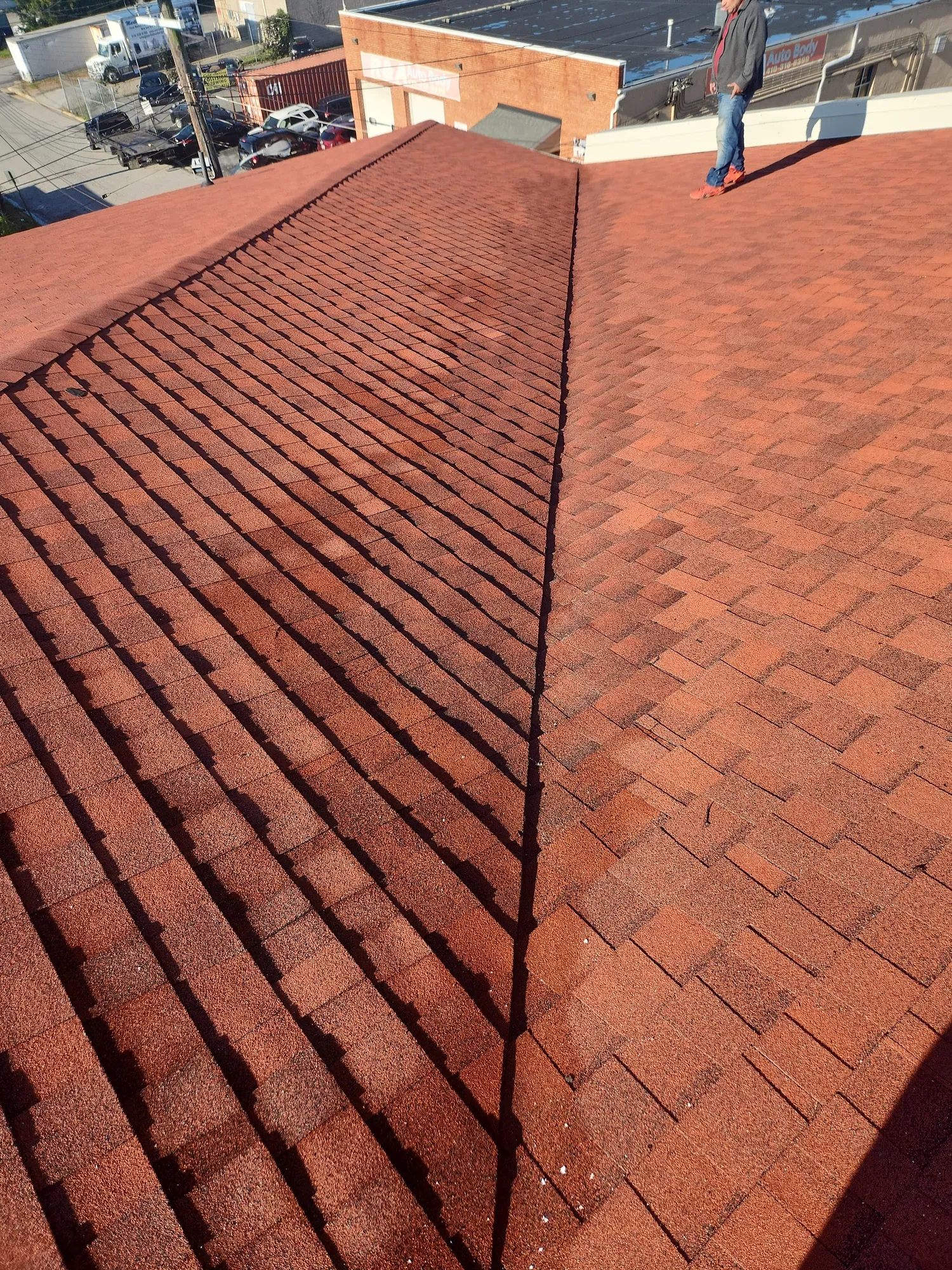 Red architectural shingle roof with a valley where two slopes meet, overlooking nearby buildings and a parking lot