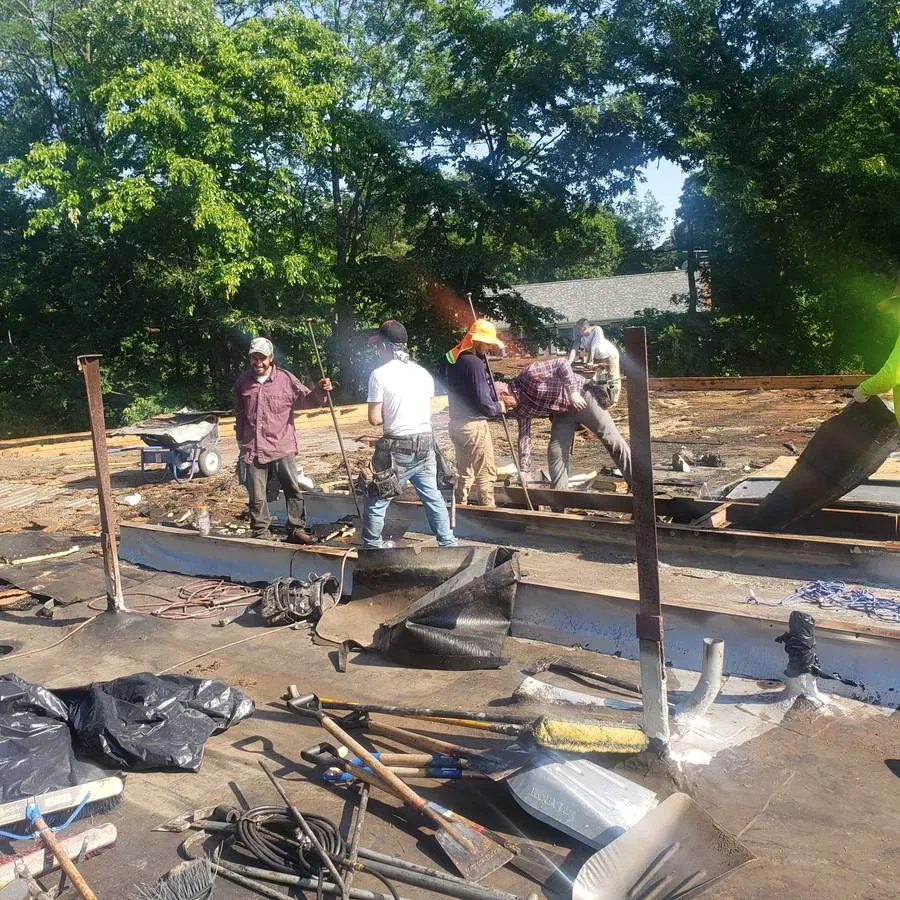 Roofing crew tearing off an old low-slope roof, with shovels and brooms in the foreground